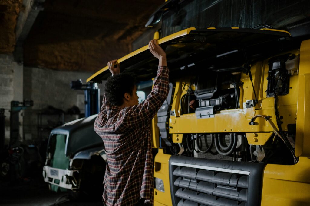 A mechanic inspecting a truck engine in a garage setting, wearing plaid shirt.